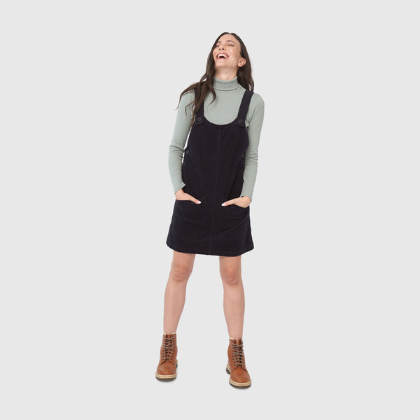 Night Sky Corduroy Overall Dress (In-use): Woman laughing, wearing dark corduroy pinafore over sage turtleneck with brown boots
