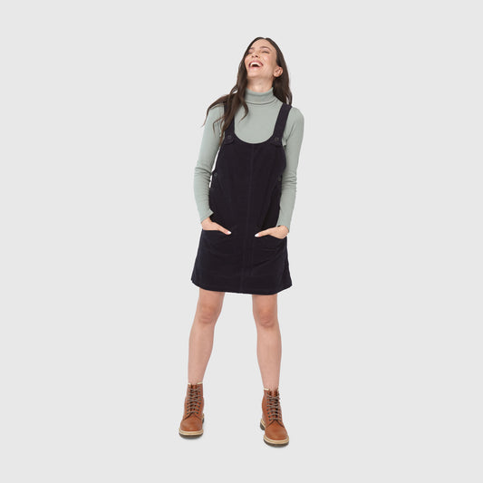Night Sky Corduroy Overall Dress (In-use): Woman laughing, wearing dark corduroy pinafore over sage turtleneck with brown boots