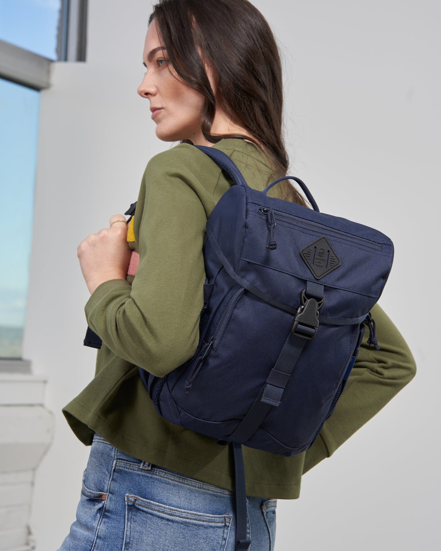 Blue W/ Green (R)evolution™ 9L Sidekick (In-use): Woman in green top wearing navy backpack with front buckle closure