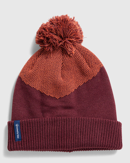 EGGPLANT Recycled Chevron Pom Beanie (Flat-lay): Deep burgundy knit beanie with orange textured chevron panel and pom-pom top