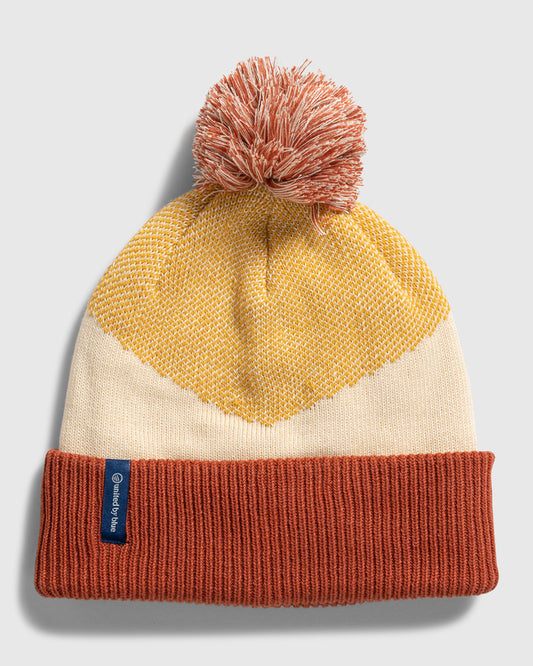 DANDELION Recycled Chevron Pom Beanie (Flat-lay): Rust cuff, cream body, mustard chevron pattern, coral pom-pom on top