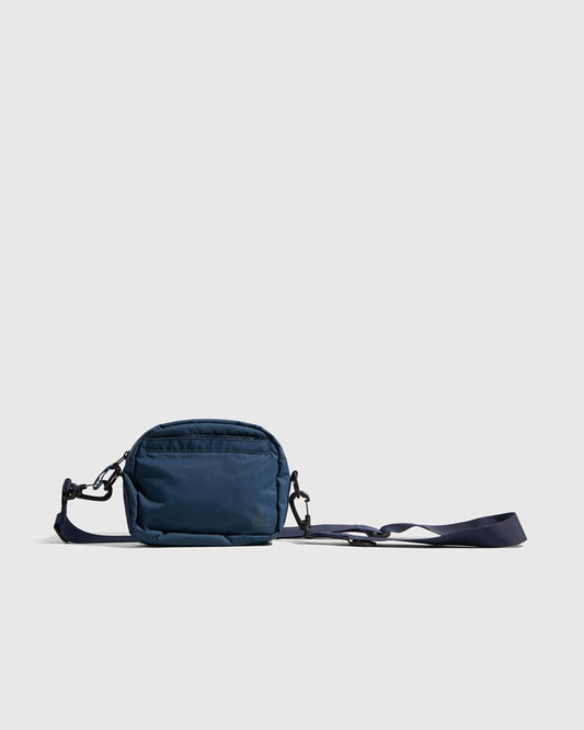 Deep Sea (Re)active™ 2L Convertible Crossbody (Angle): Navy blue crossbody bag with adjustable strap laid flat, black clips visible
