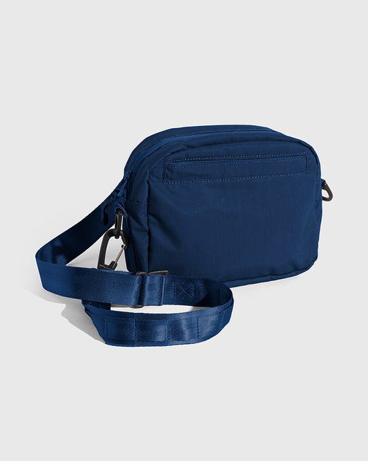 Blueberry (Re)active™ 2L Convertible Crossbody (Angle): Navy blue crossbody bag with front zip pocket and adjustable strap