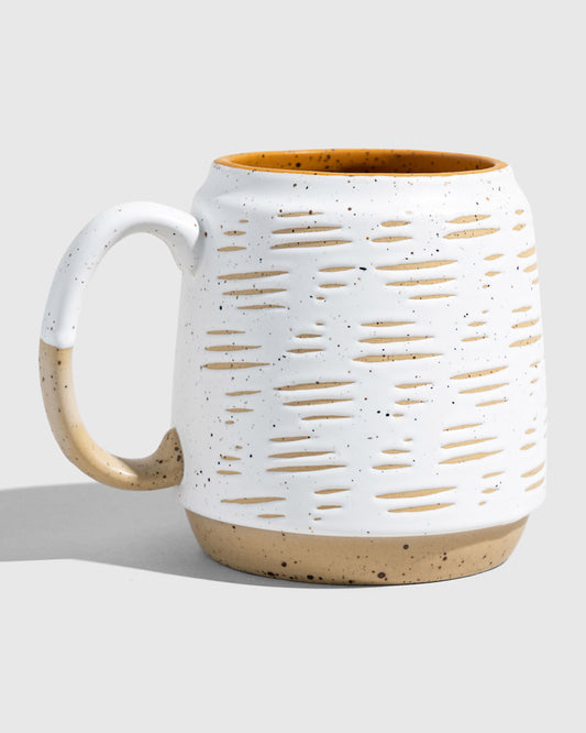 Eggshell 16 oz. Stoneware Mug (Angle): White speckled mug with oval cutout texture, tan base, mustard interior