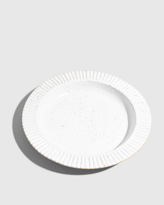 Eggshell Stoneware Stackable Plate (Angle): Round white speckled plate with ribbed fluted rim, unglazed edge visible