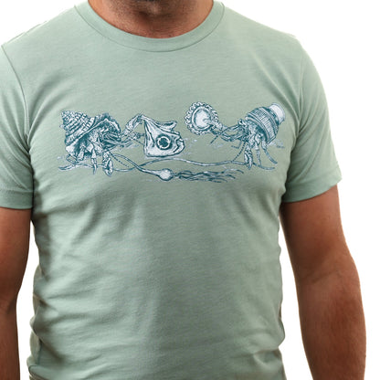 Heather Sage What We Save Graphic Tee - Slow Loris x United By Blue (Detail): Light green tee with hermit crabs carrying trash as makeshift shells