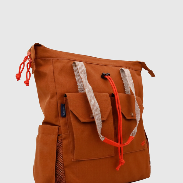 Rustic Caramel (R)evolution™ 27L Utility Convertible Tote (Angle): Burnt orange tote with herringbone handles, red rope pulls, and front flap pockets