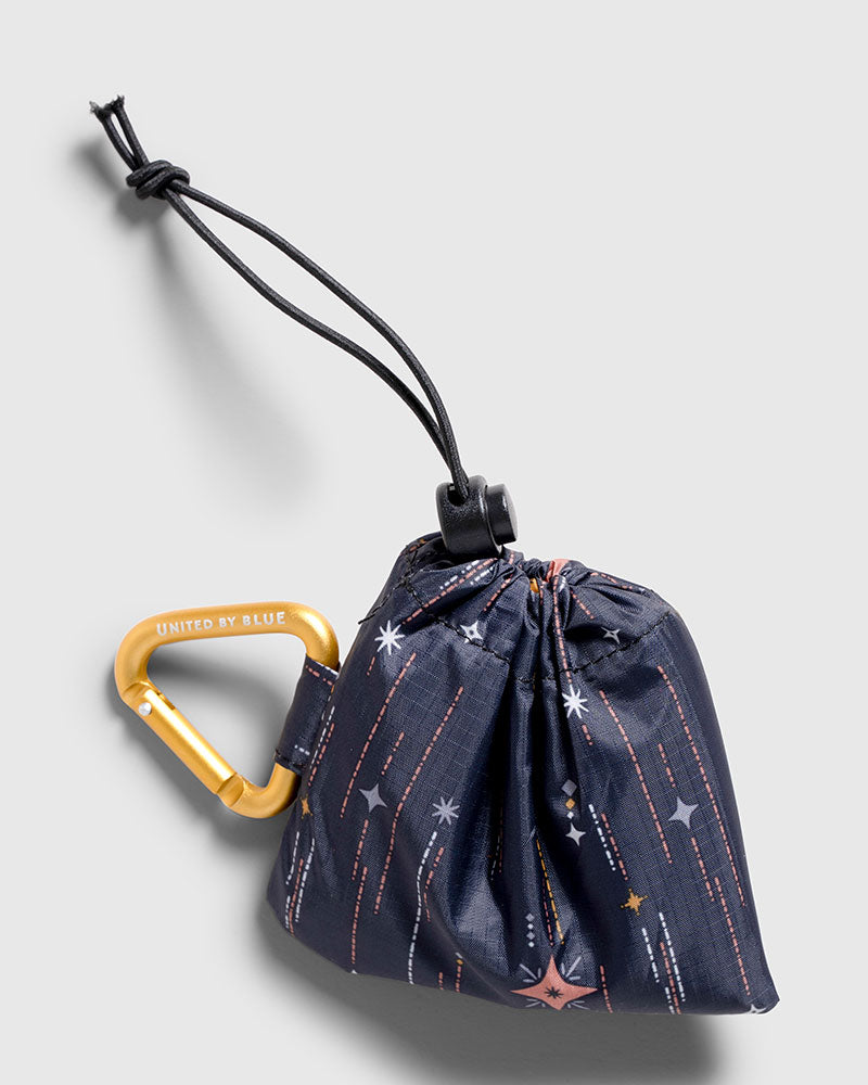 Night Sky The Packable Tote (Detail): Navy star-print pouch with gold carabiner clip and drawstring closure