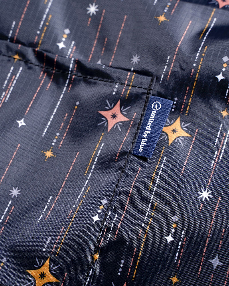 Night Sky The Packable Tote (Detail): Close-up of dark fabric with stars and streaks, showing brand label