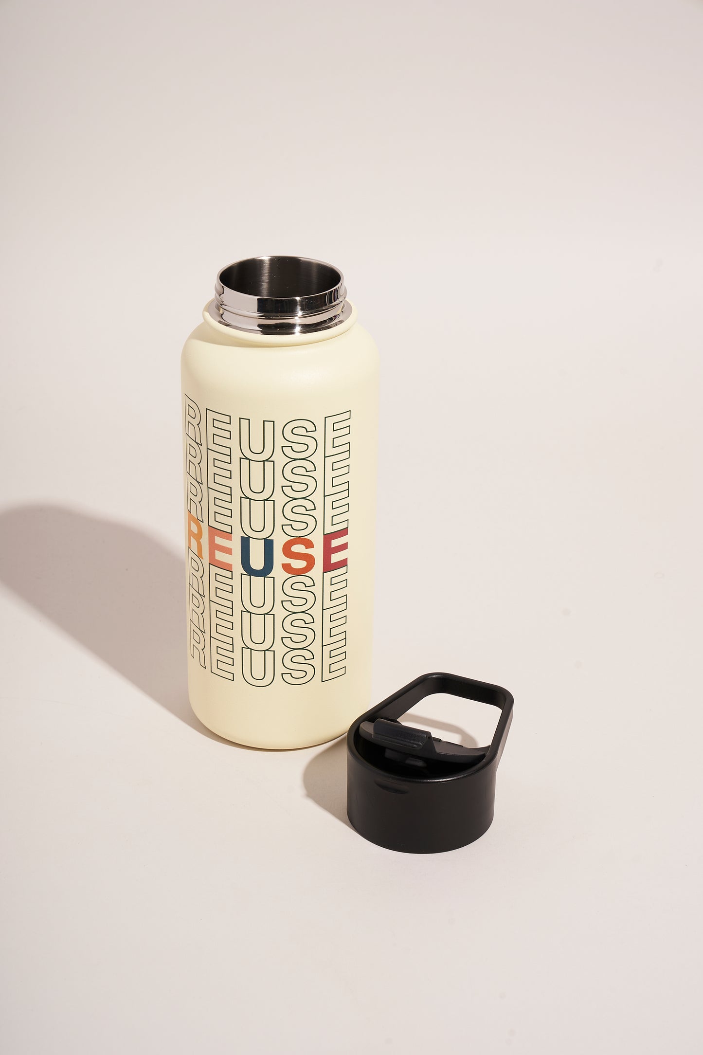Eggshell - Reuse Bottle - 23 Oz. Insulated Stainless Steel (Angle): Cream stainless steel bottle with multicolor REUSE text pattern, lid removed