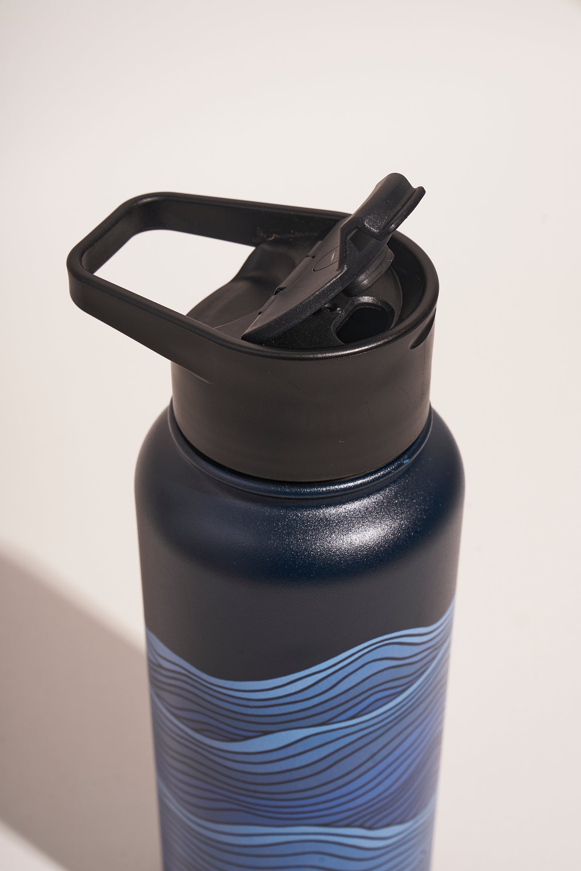 Lake - Waves Bottle - 23 Oz. Insulated Stainless Steel (Detail): Close-up of black flip-top lid and carry handle on dark navy bottle with blue wave pattern