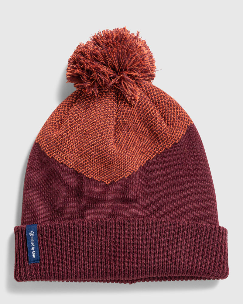 Eggplant Recycled Novelty Pom Beanie (Flat-lay): Deep burgundy knit beanie with orange textured chevron panel and pom-pom top