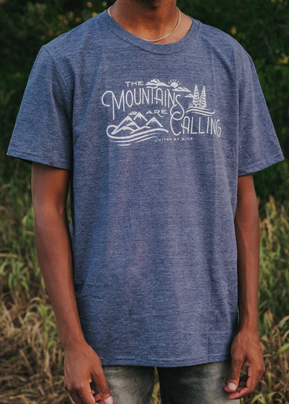 Heathered Navy Mountains Are Calling - Biodegradable Graphic Tee - (All-gender) (In-use): Dark blue heathered tee with white mountain scene graphic, worn outdoors