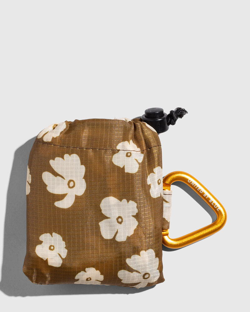 Smoky Ochre The Packable Tote (Detail): Brown floral pouch with white flowers, drawstring top, and gold carabiner clip