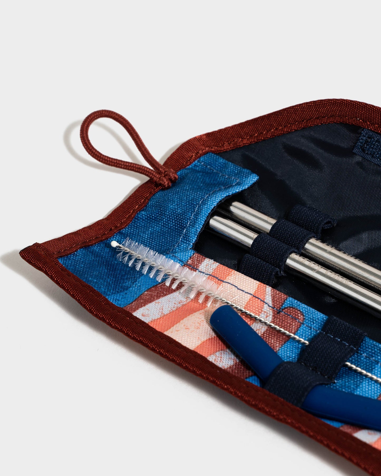 The Straw Kit (Detail): Open roll case revealing steel straws, cleaning brushes, and blue silicone tip