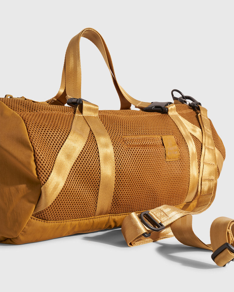 (Re)active™ 16L Mini Duffle (Detail): Golden tan mesh duffle with webbing straps, black buckles, and logo patch