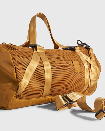 (Re)active™ 16L Mini Duffle (Detail): Golden tan mesh duffle with webbing straps, black buckles, and logo patch