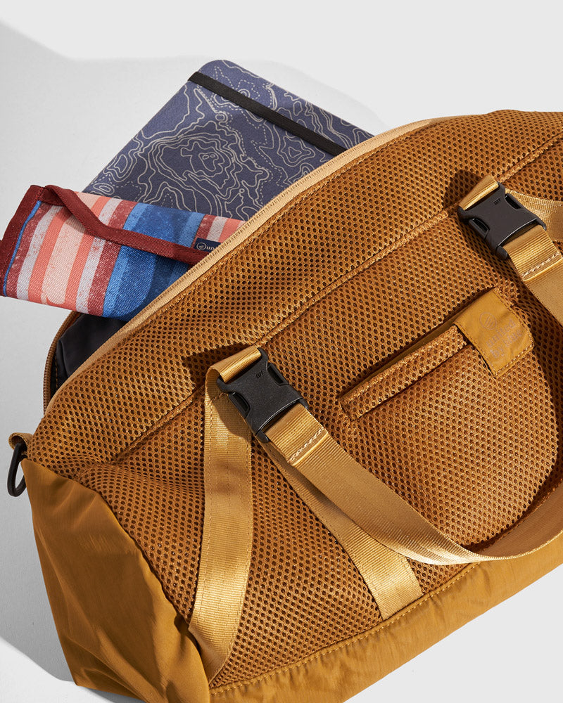 (Re)active™ 16L Mini Duffle (Detail): Tan mesh duffle bag open, showing buckle straps, front pocket, and folded items inside