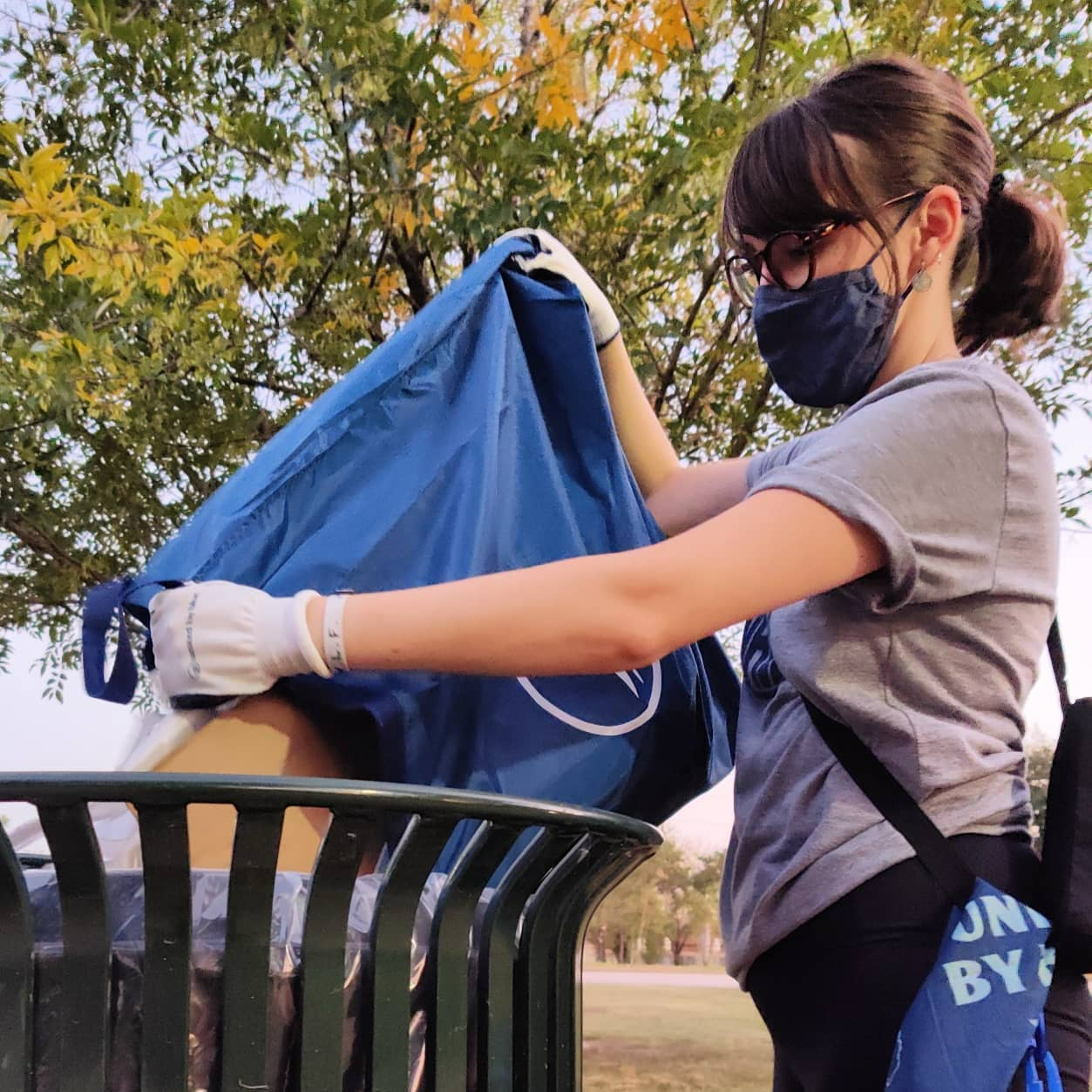 Navy Reusable DIY Cleanup Kit (In-use): Person with gloves and mask empties navy blue bag into outdoor trash can