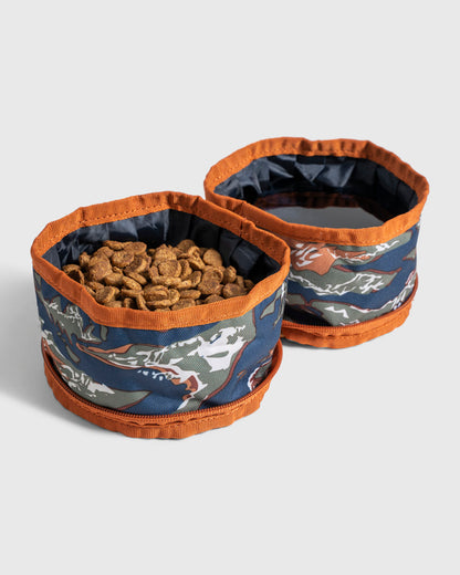 (R)evolution™ Collapsible Double Dog Bowl (Angle): Two collapsible fabric bowls with blue camo print and orange trim, one filled with kibble