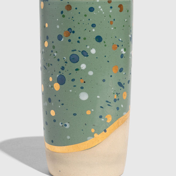Juniper 10 oz. Insulated Stoneware Travel Mug (Angle): Sage green speckled mug with blue, white, gold dots and bare clay base