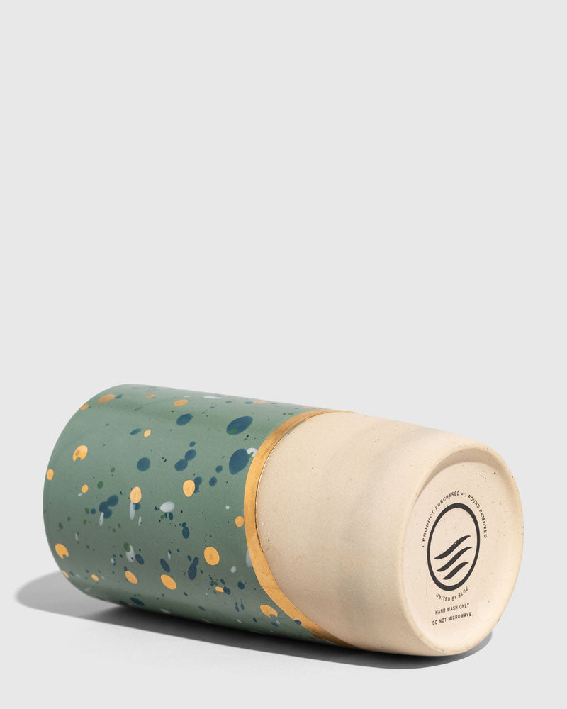 Forest Floor 10 oz. Insulated Stoneware Travel Mug (Detail): Green speckled mug on its side showing unglazed ceramic base with logo