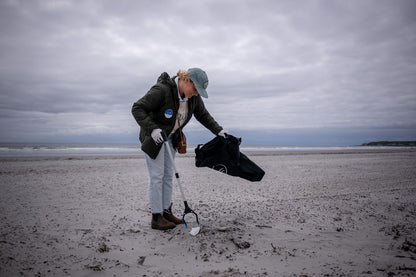 Reusable DIY Cleanup Kit (In-use): Person collecting beach litter with grabber tool and black trash bag