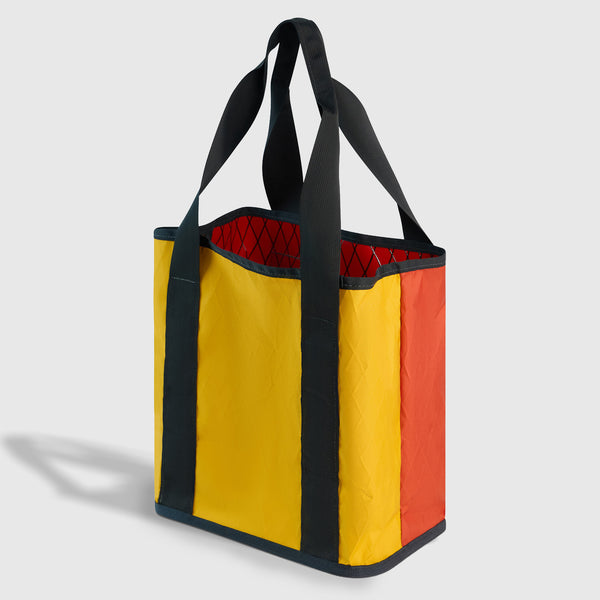 Coral Red The Westward Tote (Angle): Yellow and orange tote with dark straps and red quilted interior visible