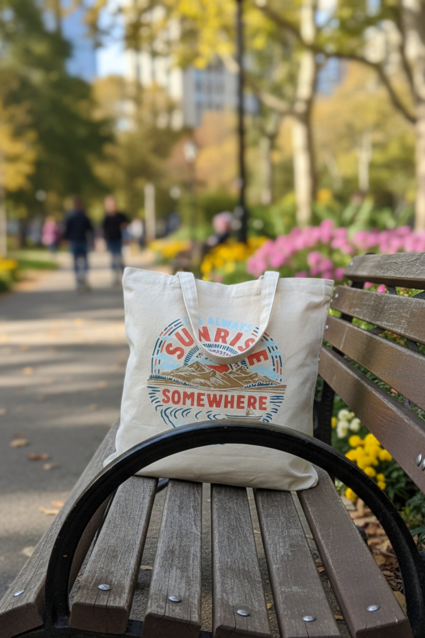 It's Always Sunrise Somewhere My Favorite Daily Tote (Lifestyle): Cream canvas tote with mountain sunrise print rests on park bench