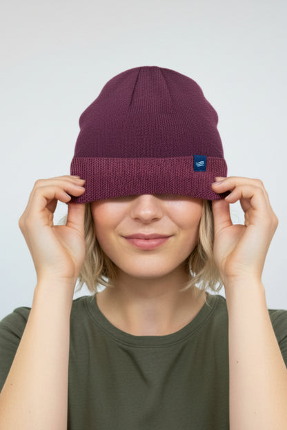 Burgundy The Essential Merino Marled Beanie (In-use): Person smiling, pulling burgundy knit beanie down over their eyes