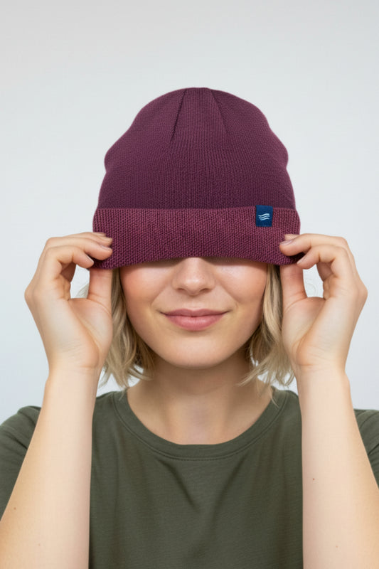 Burgundy The Essential Merino Marled Beanie (In-use): Smiling woman pulls burgundy knit beanie down over her eyes, blue logo patch visible