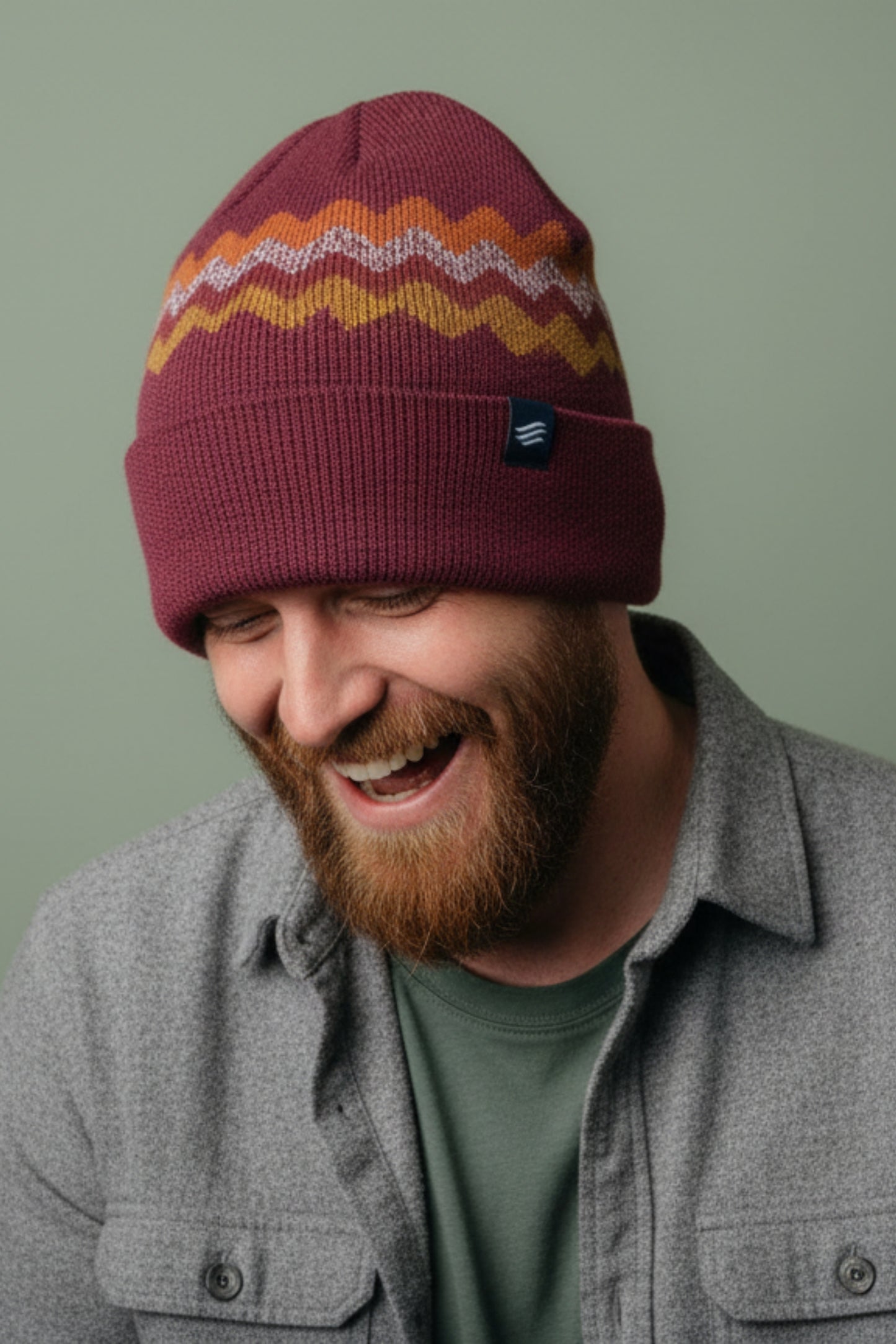 Burgundy Merino Wool Mountain Scape Knit Beanie (In-use): Smiling bearded man wearing dark red beanie with orange and yellow zigzag pattern