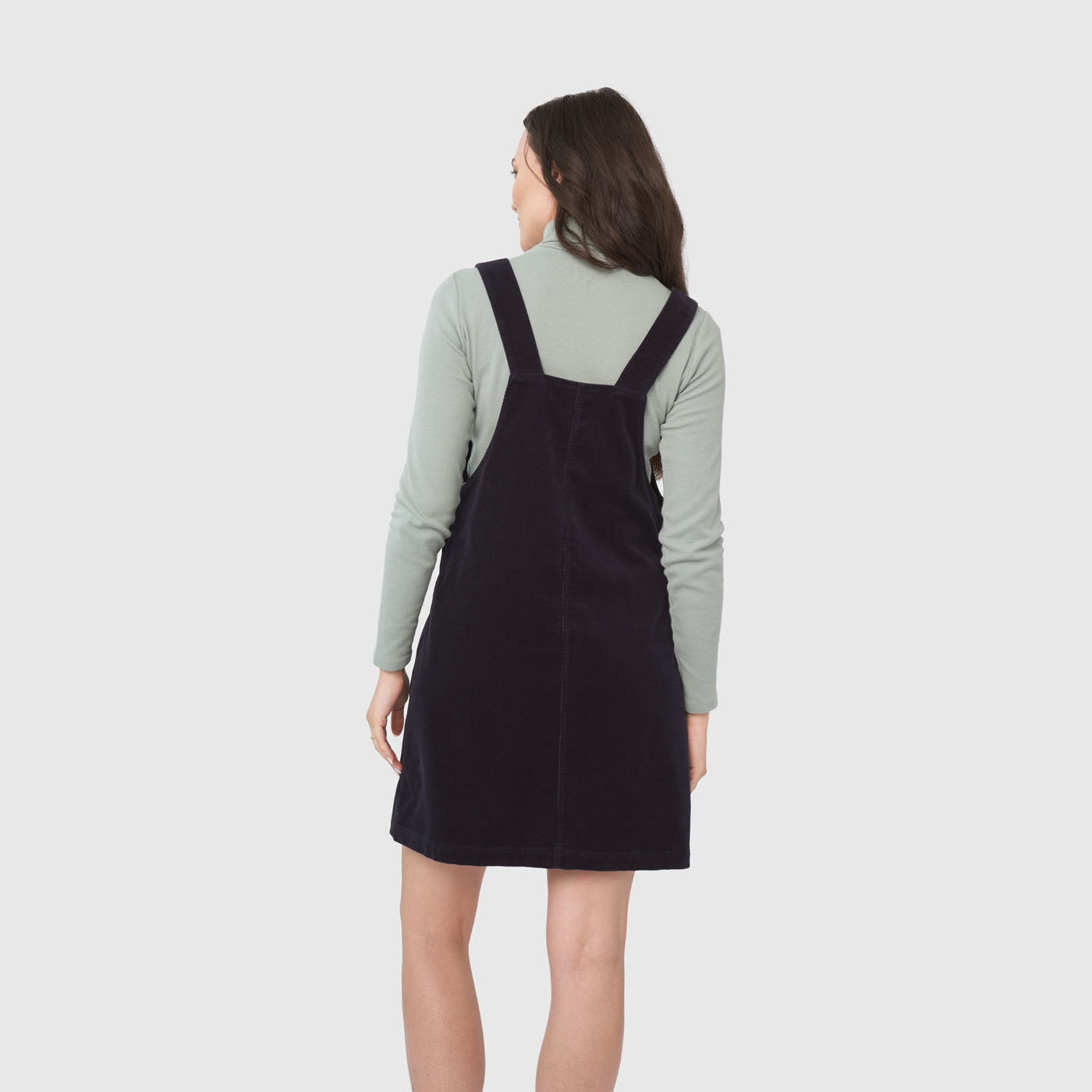 Night Sky Corduroy Overall Dress (Back): Dark navy corduroy pinafore dress with wide straps, worn over mint turtleneck
