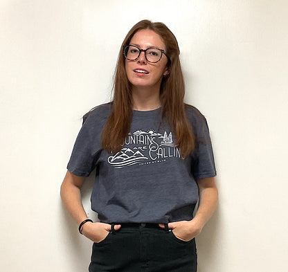 Heathered Navy Mountains Are Calling - Biodegradable Graphic Tee - (All-gender) (In-use): Dark blue tee with white mountain graphic worn by young woman with glasses