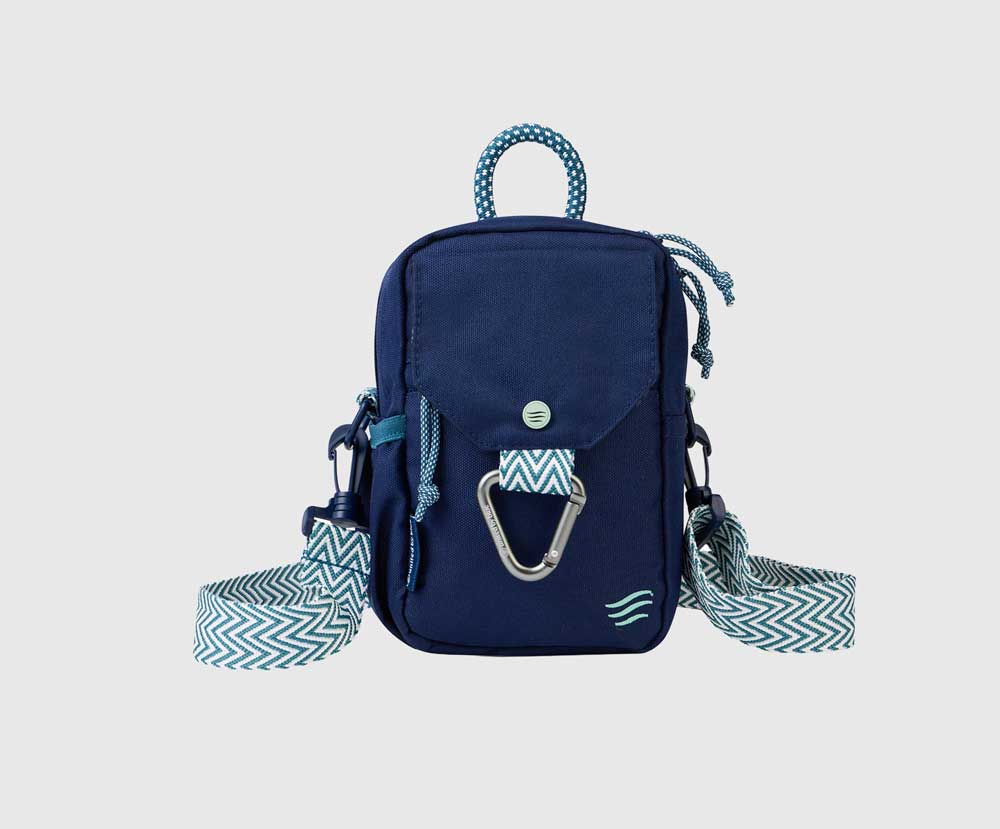 Navy (R)evolution Daily Cross Body (Front): Navy crossbody bag with mint accents, silver carabiner, snap-flap pocket, and zigzag chevron strap