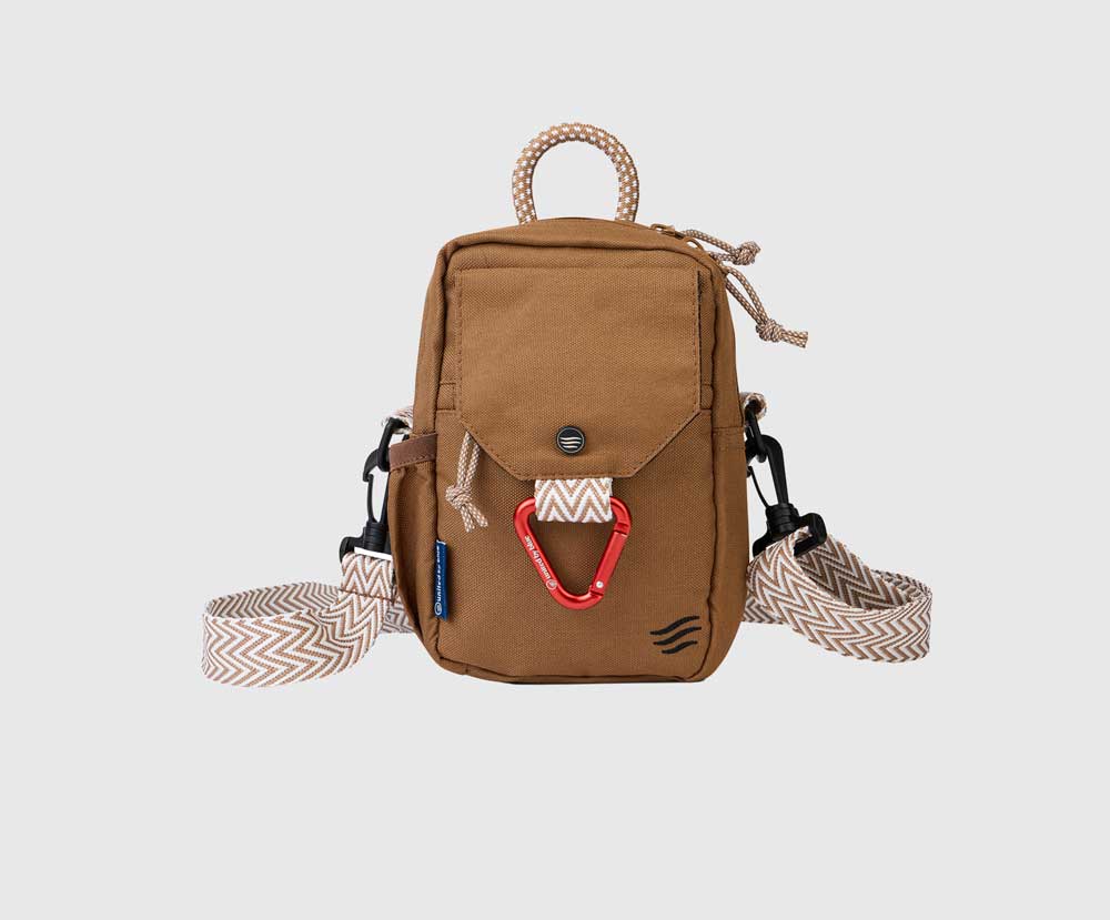 Tigers Eye (R)evolution Daily Cross Body (Front): Tan brown crossbody bag with snap-flap pocket, red carabiner, rope handle, and chevron strap