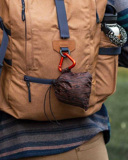 Waves The Packable Tote (In-use): Dark wave-print pouch clipped via red carabiner to tan backpack