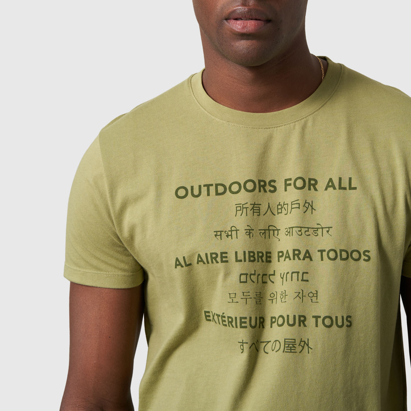Sage Outdoors For All Graphic Tee (Detail): Close-up of olive green tee with multilingual outdoor slogan printed on chest