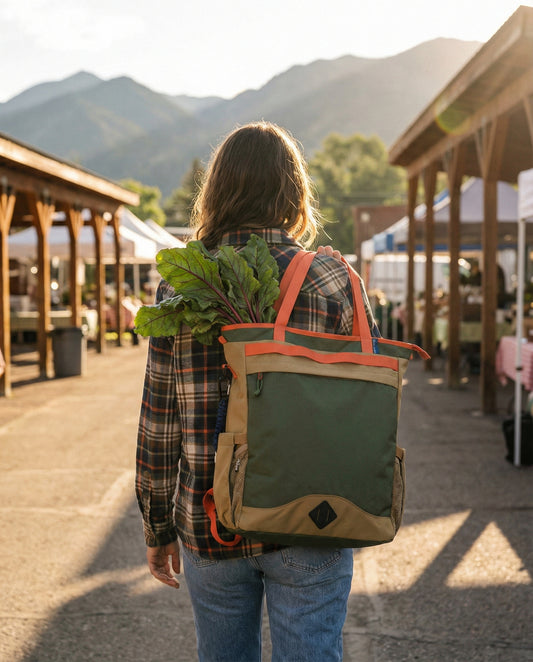 Green Multi (R)evolution™ 25L Convertible Carryall (In-use): Person wearing olive and tan backpack tote at outdoor farmers market