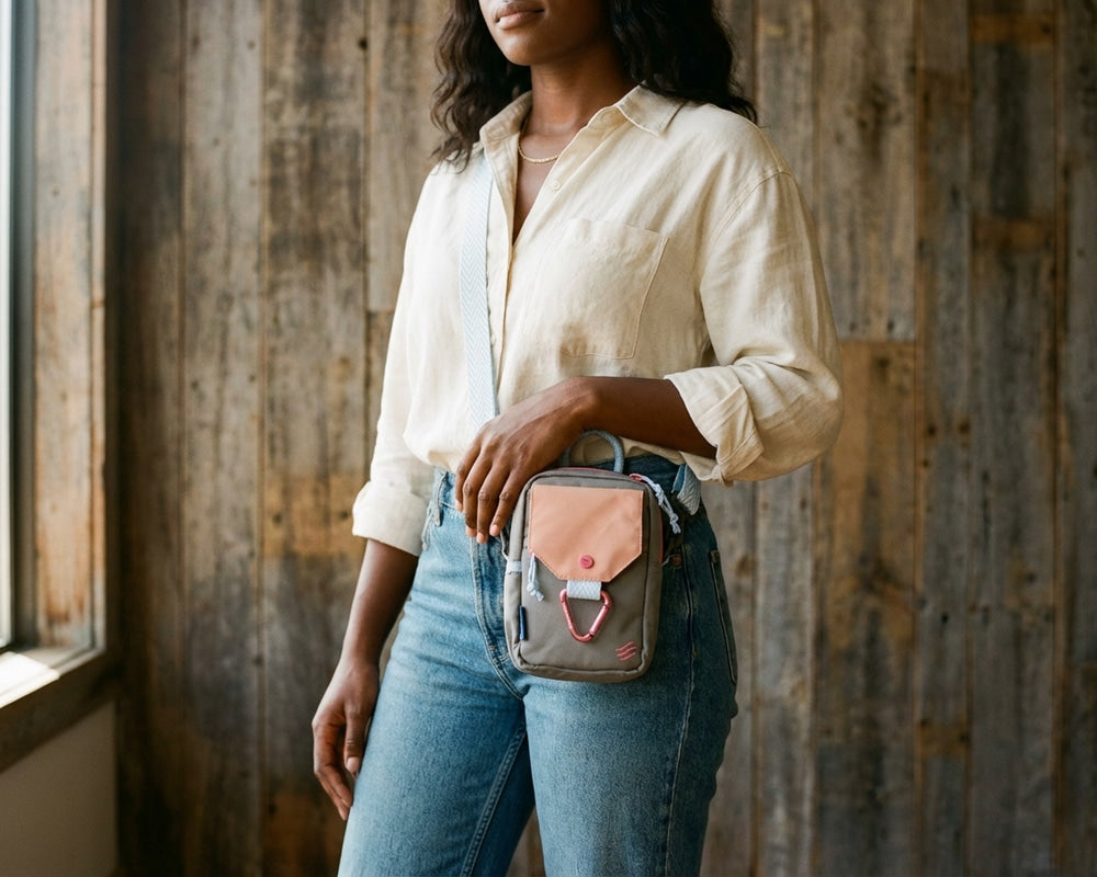 Lt Grey Bag - Person holding a small crossbody bag against a wooden wall.