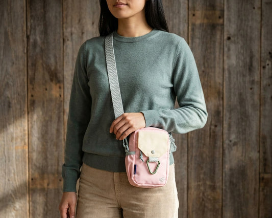 Lt Pink (R)evolution™ Daily Cross Body (In-use): Woman wearing pink and cream crossbody bag with patterned strap, wooden background