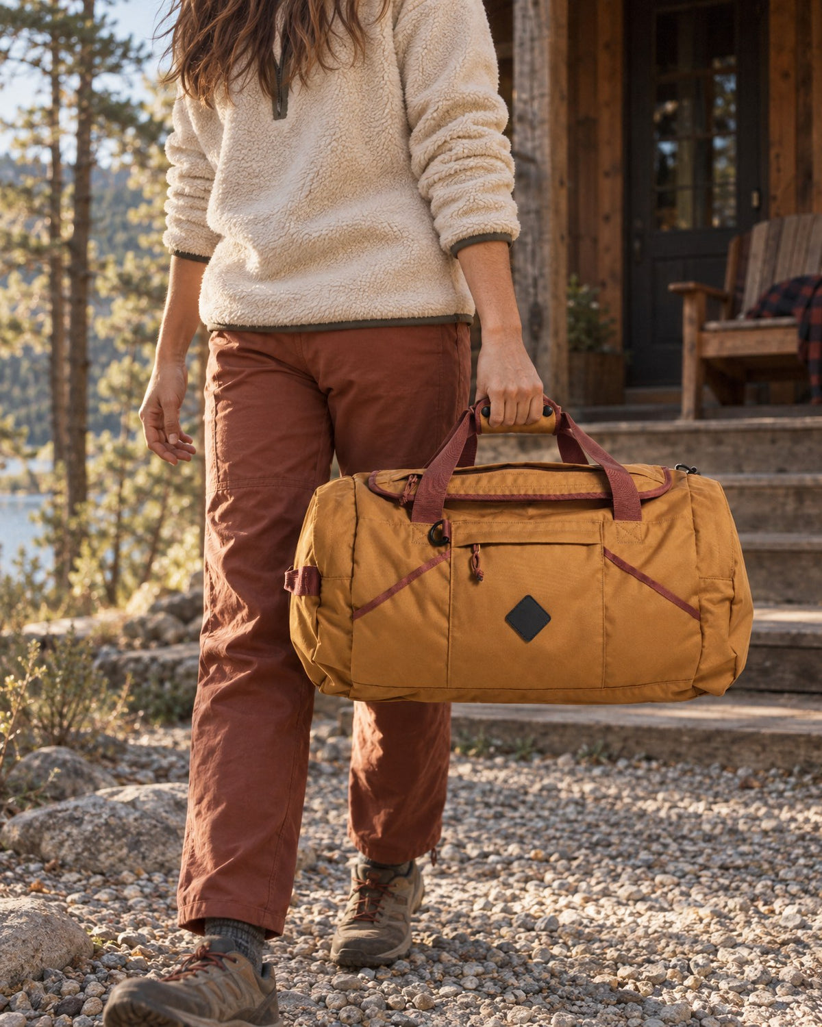 Woman walking up a gravel path to a cabin carrying the camel (R)evolution 55L Carry-On Duffle by its handles