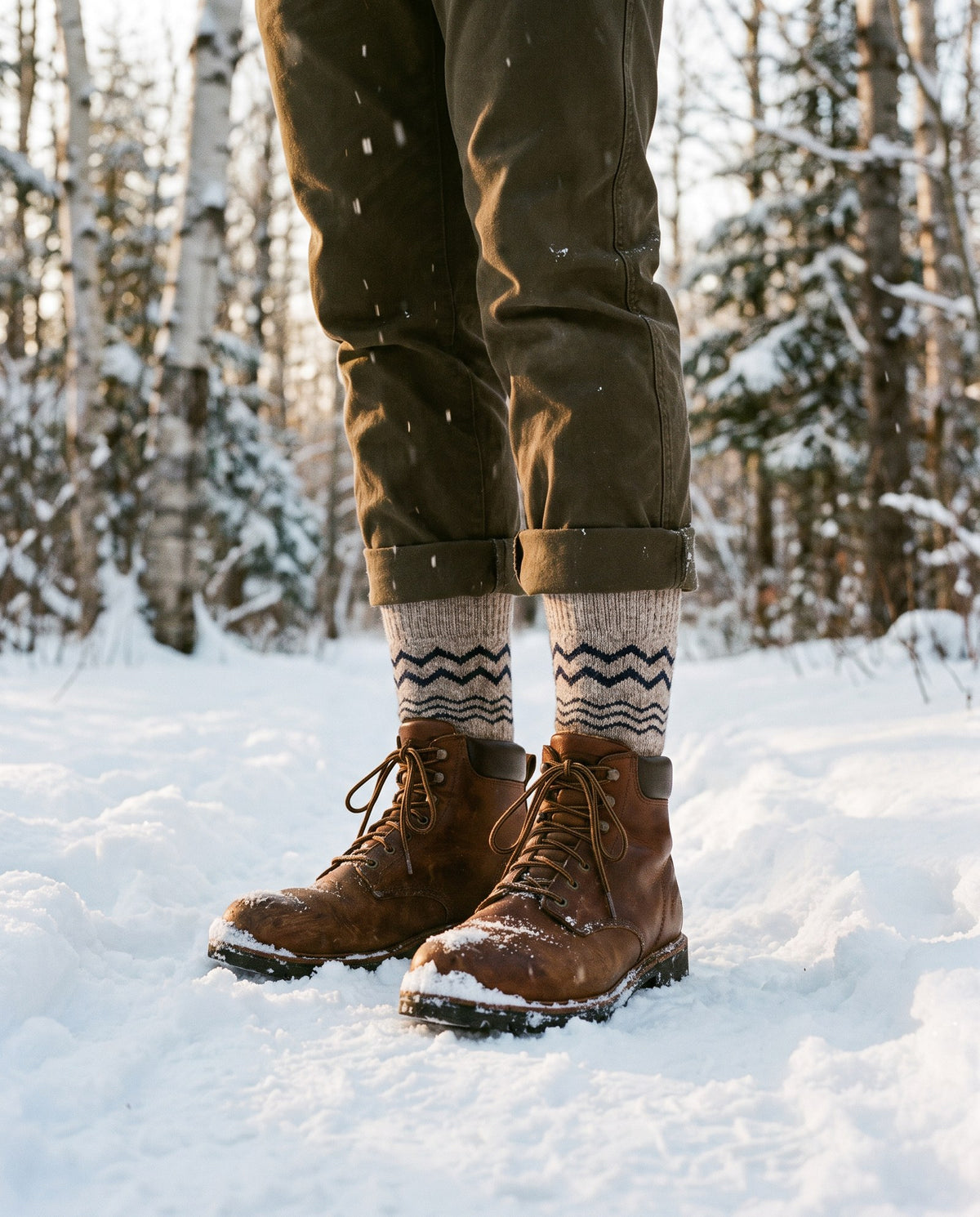 Hiker standing in fresh snow in brown leather boots, with the navy zigzag band of the Ultimate Bison Wool Sock showing above the boots