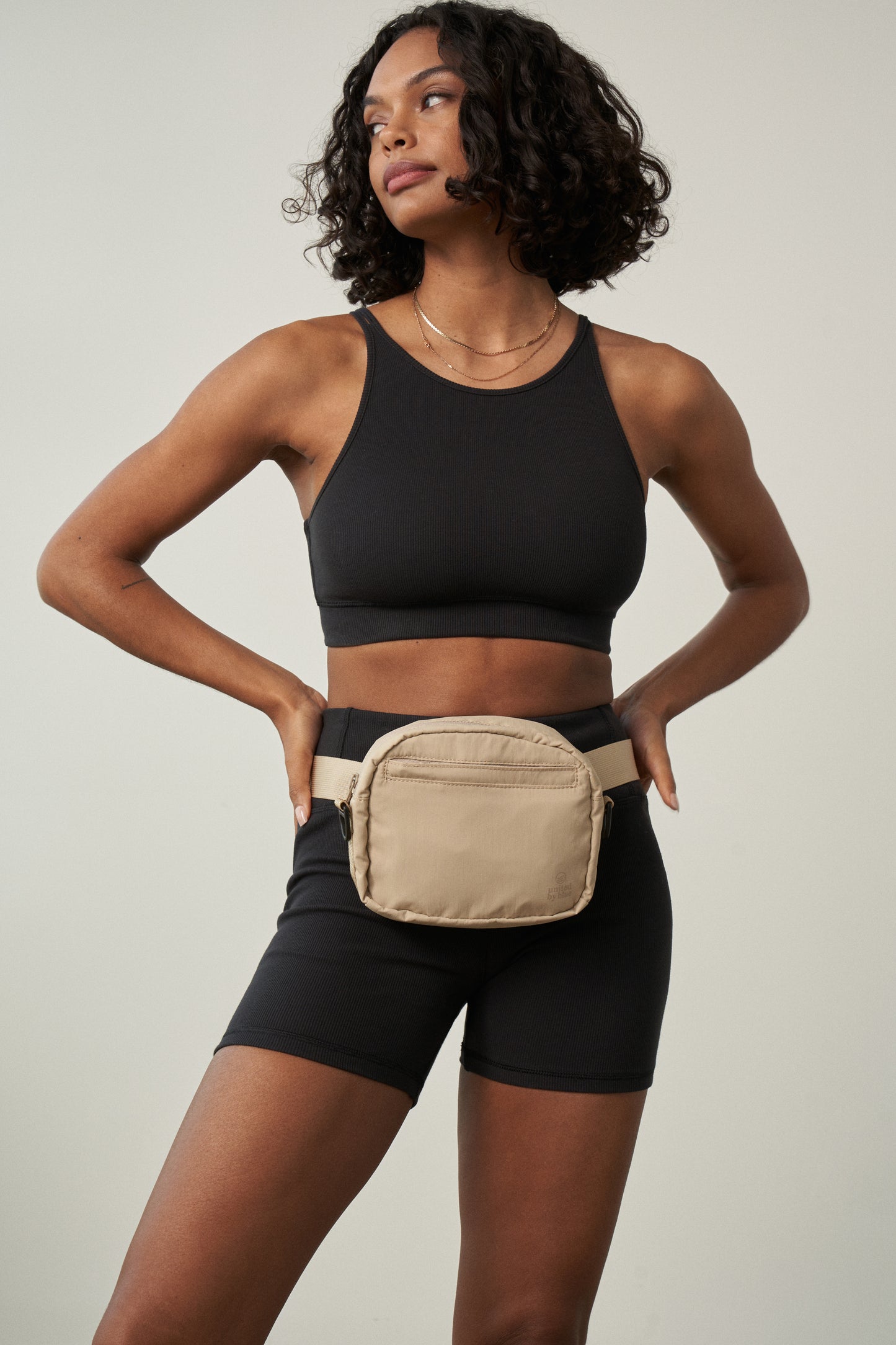 Sand (Re)active™ 2L Convertible Crossbody (In-use): Light tan belt bag worn at waist by woman in black athletic wear