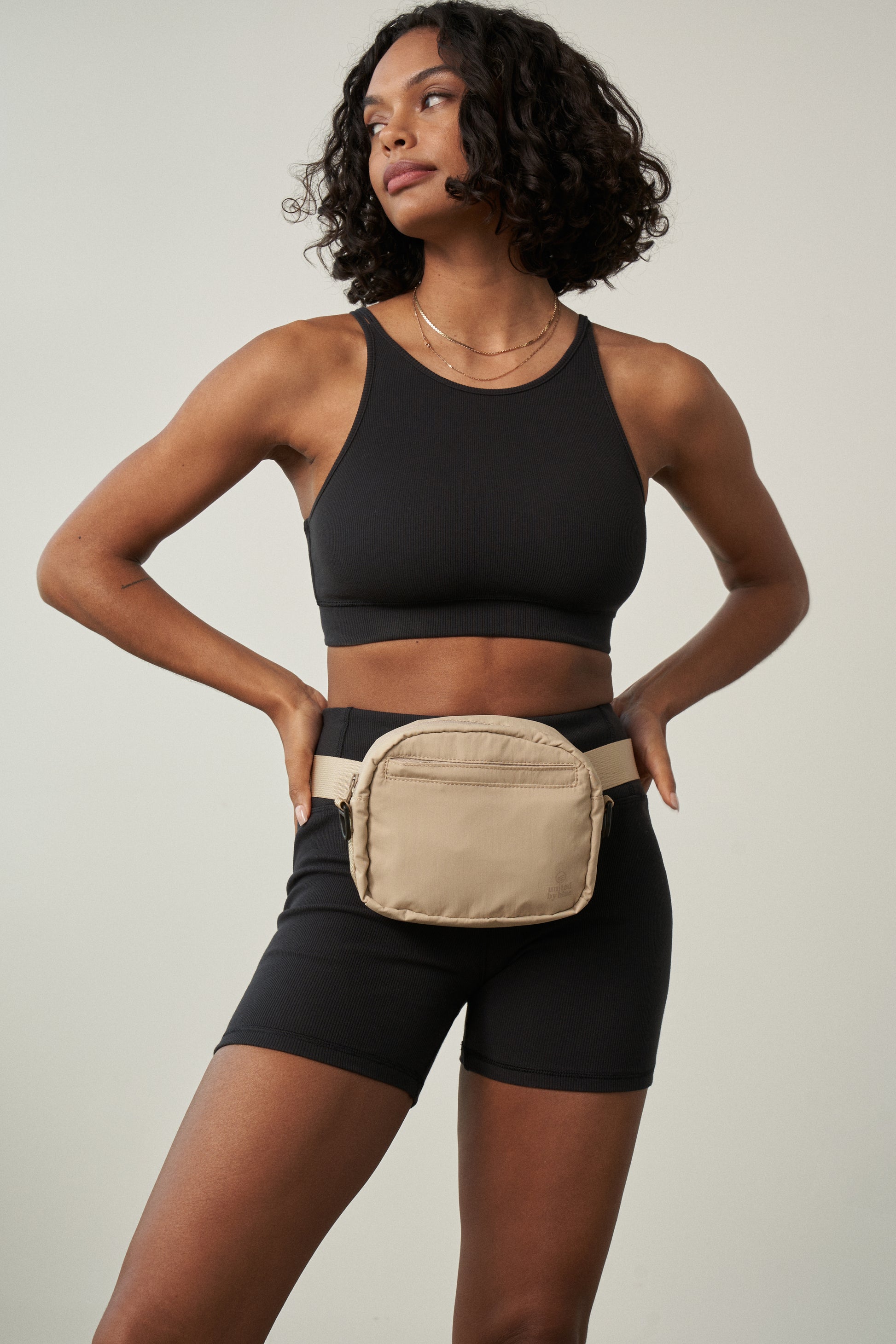 Sand (Re)active™ 2L Convertible Crossbody (In-use): Light tan belt bag worn at waist by woman in black athletic wear