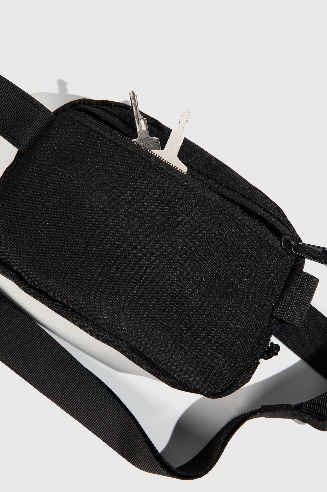 Black (Re)volution™ 1L Go-Anywhere Bag (Detail): Black canvas bag with front zipper pocket and silver keys tucked inside