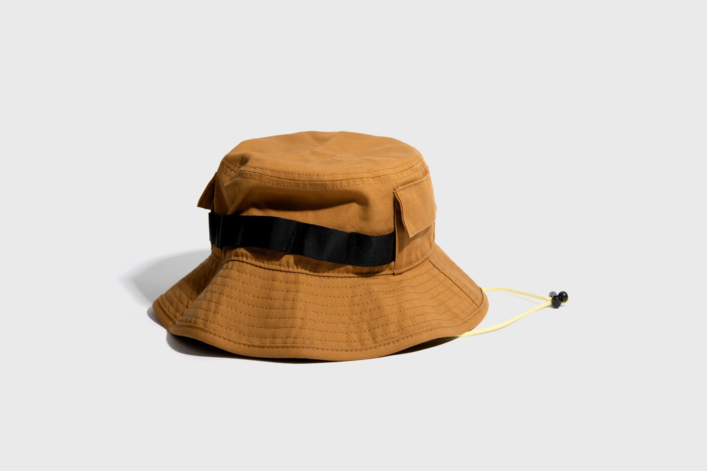 HONEY UTILITY BUCKET HAT (Angle): Golden-brown bucket hat with black webbing band, yellow chin cord, side pocket