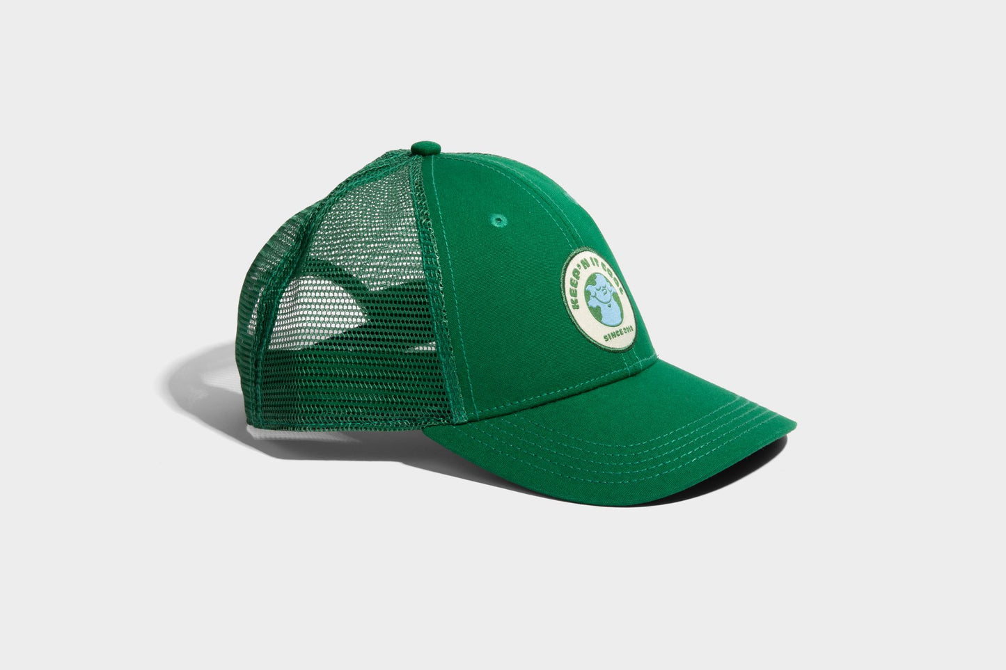 PINE ORGANIC TRUCKER HAT (Angle): Green trucker cap with mesh back and circular earth patch logo