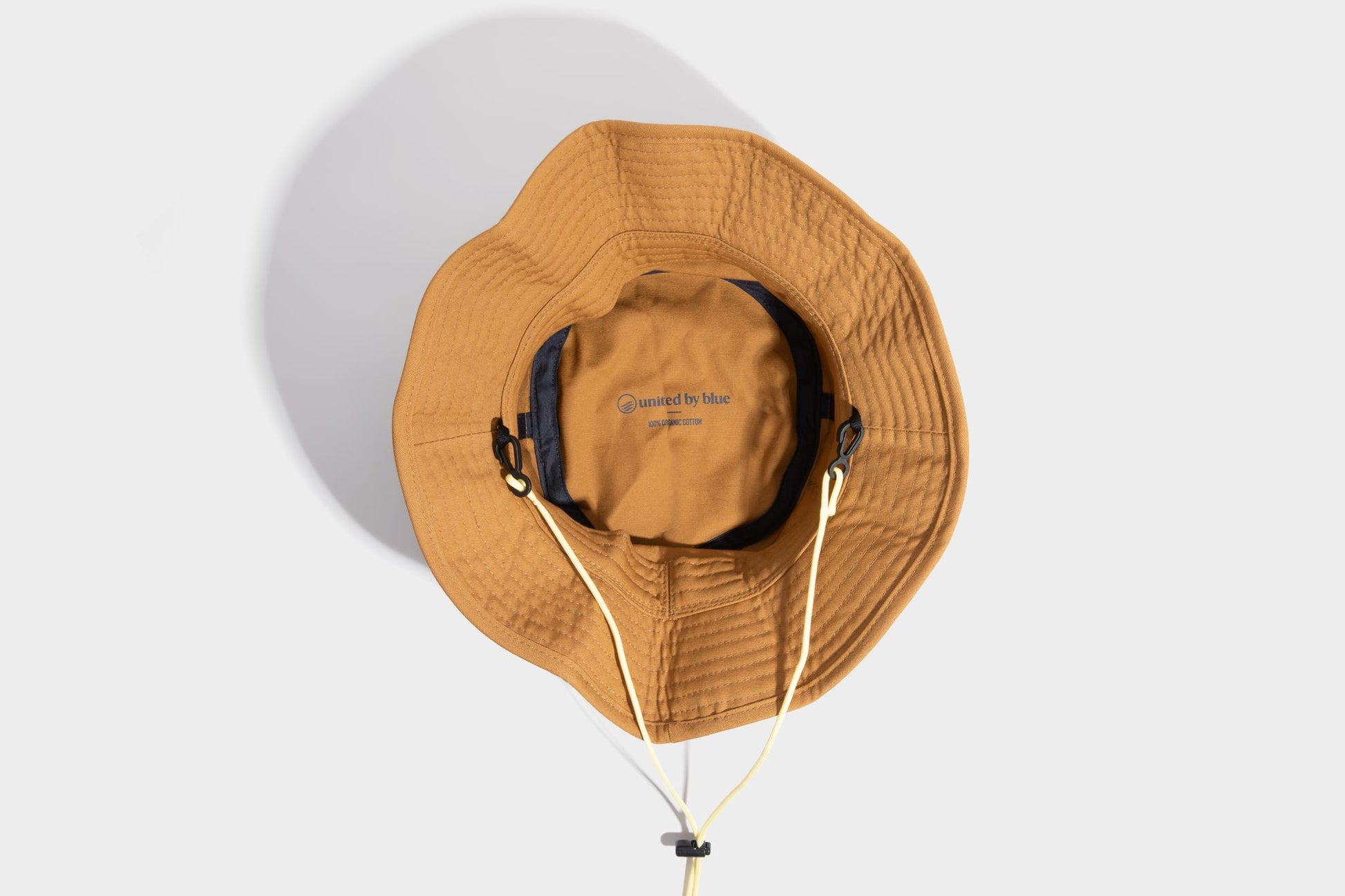 HONEY UTILITY BUCKET HAT (Detail): Interior view of amber bucket hat showing label, chin cord, and clips