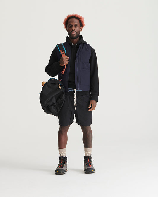 Black Recycled Sport Short (In-use): Man wearing black drawstring shorts with hiking boots and navy vest